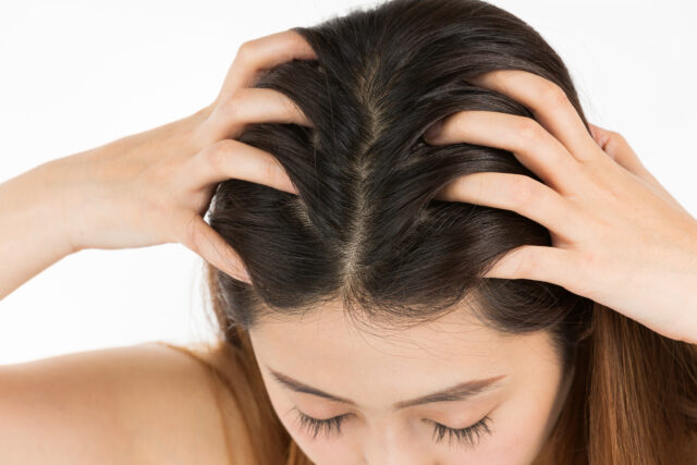 自分の頭皮を優しくマッサージしているロングヘアの女性